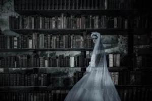 An image of a ghost, dressed as a bride, in front of library book stacks